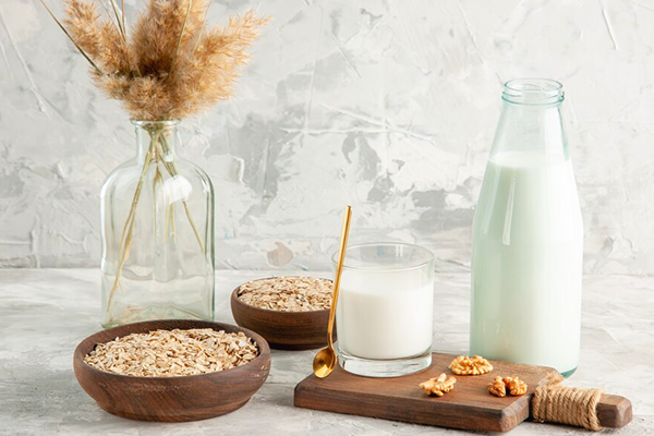 2 bowls of oat, 1 glass jug and a cup contain milk,
