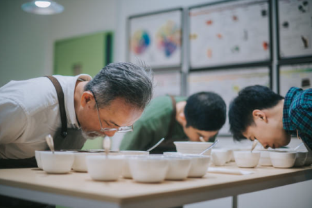 A team of adults adorning aprons smelling a collection of bowls for testing purposes.
